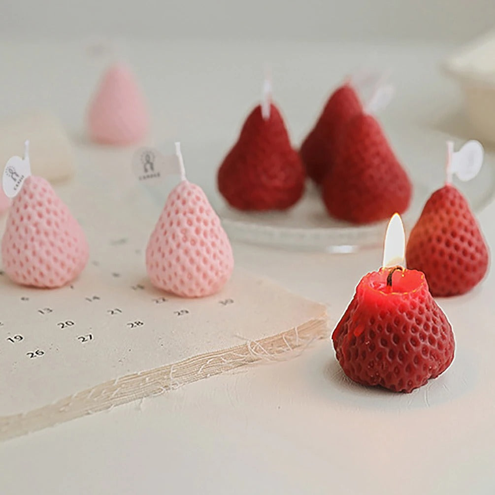 Five red and three pink strawberry shaped candles. One of the red strawberry candles is alight with a flame.