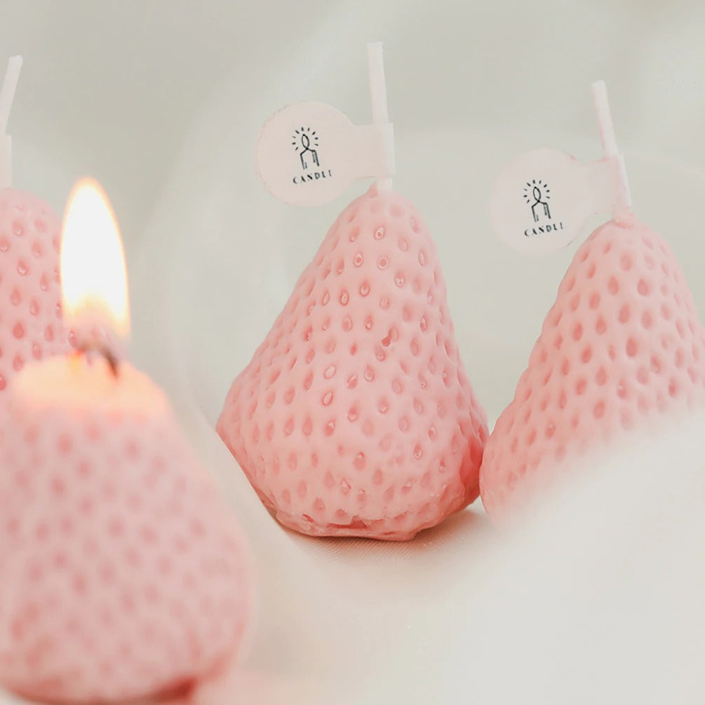 A close up of four pink strawberry shaped candles. One is alight and the others are flameless.