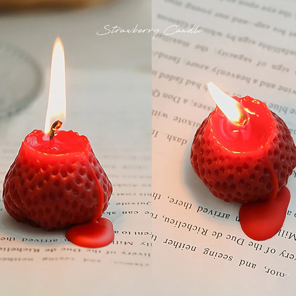 Two red strawberry shaped candles half melted and alight.