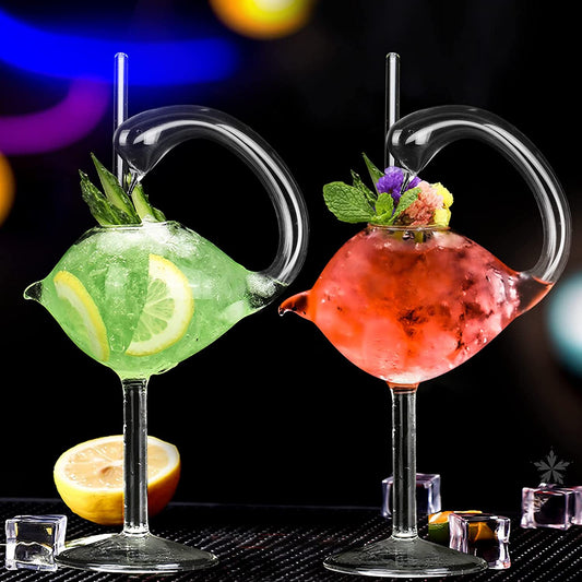 Two cocktail glasses shaped like swans with matching glass straws. One has a green drink in it and the other has a red drink in it. 