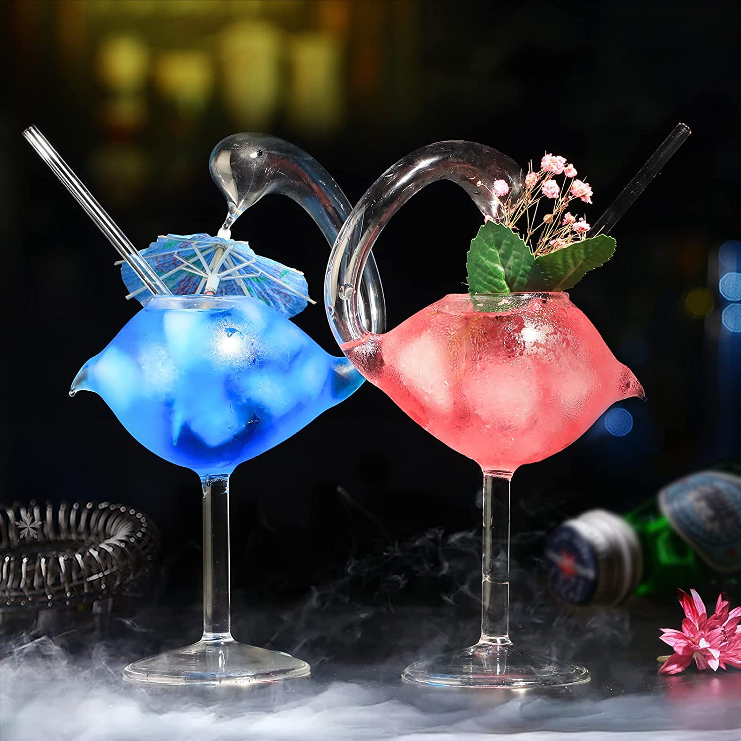 Two swan shaped cocktail glasses. One has a blue drink with a cocktail umbrella in it and the other has a red drink in it with a floral garnish.