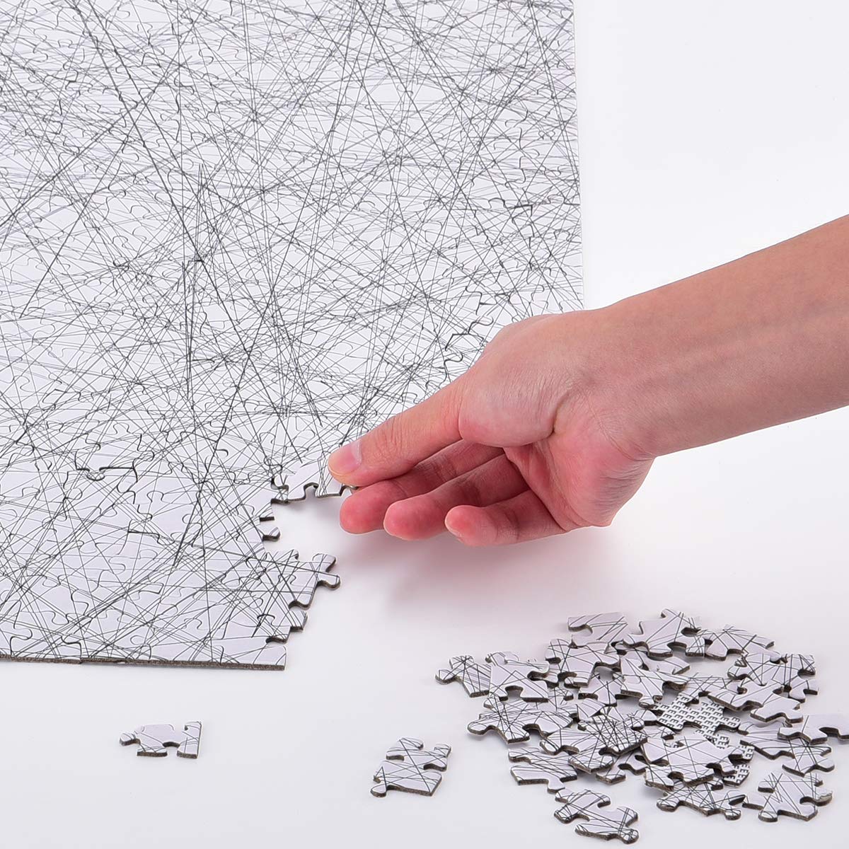 A hand holding a jigsaw piece and putting together a 1000 piece jigsaw puzzle made up of hundreds of straight black lines criss crossed over each other.