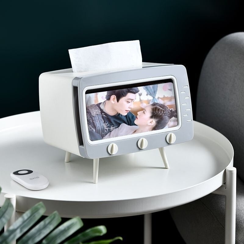 A white and grey tissue box shaped like a TV set resting on a table