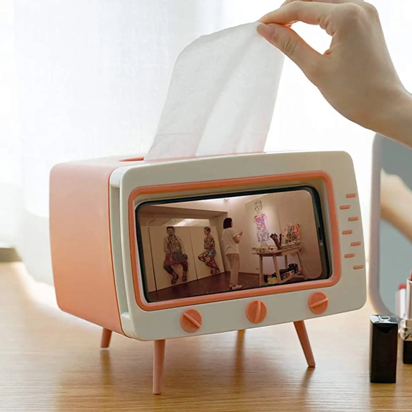 A tissue box which is shaped like a Tv and get hold your phone is you can watch videos. A hand is pulling a tissue out of the top of it.