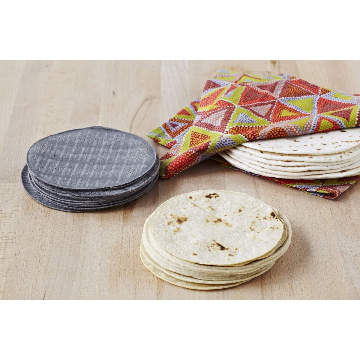 Two stacks of freshly cooked tortillas with a pile of grey placemats nearby.