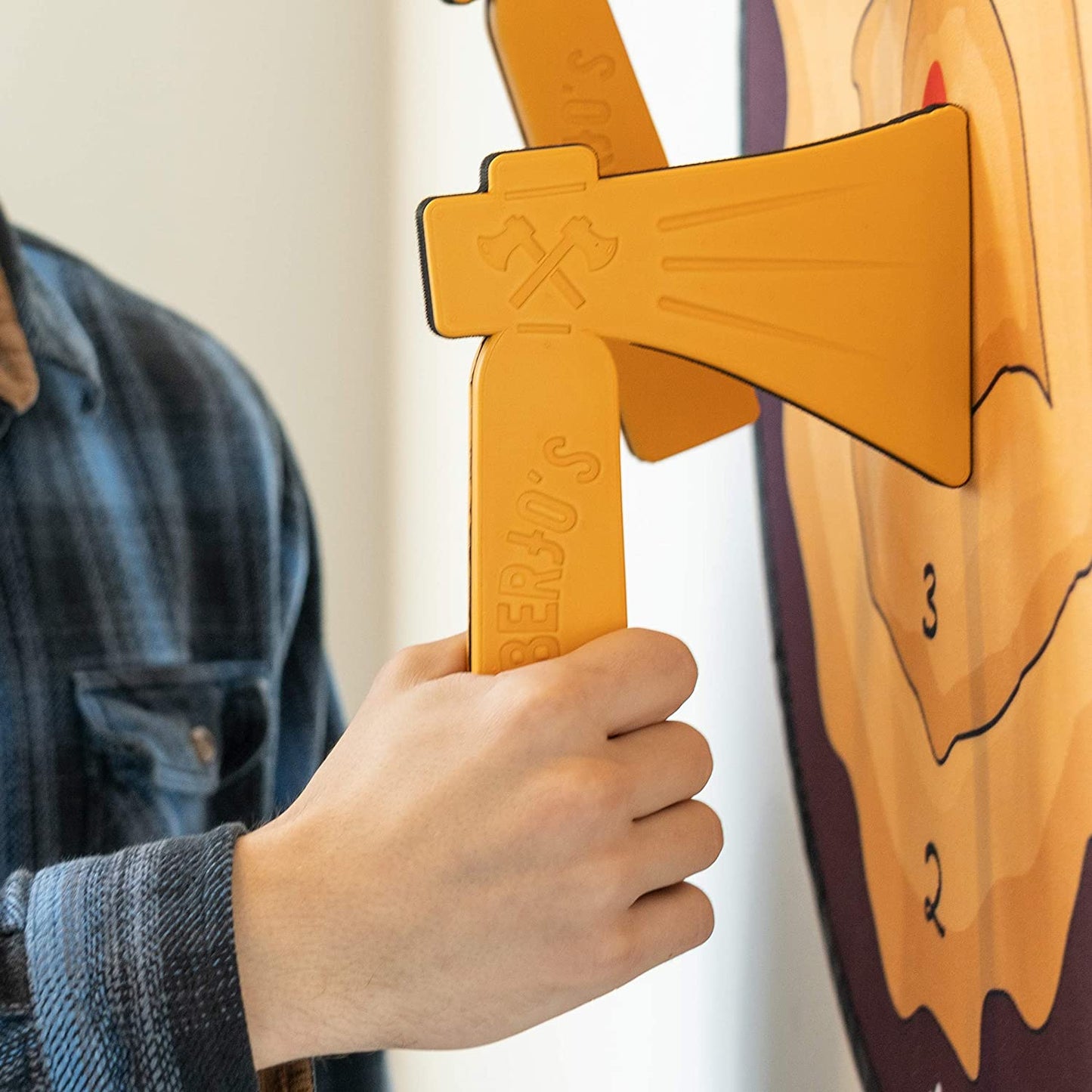 A hand is grabbing onto a foam axe which is sticking out of a bullseye board.