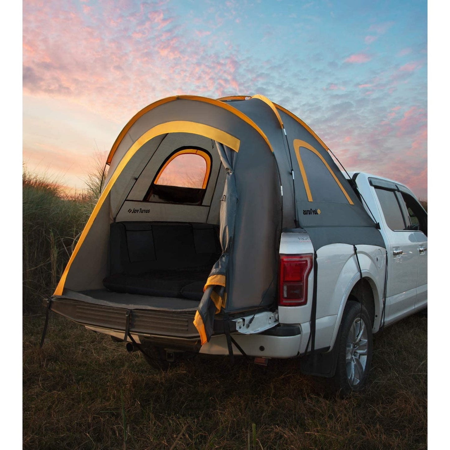 A two person pickup truck tent is attached to the back of a white pickup truck in the great outdoors.