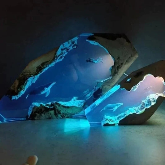 Two desk lamps which look like a slice of underwater life. One lamp is larger than the other. The lights are switched on in both lamps and they are both emitting a soft blue light. There is a diver and a humpback whale swimming toward each other in an underwater cave which looks lit up by sunshine from above.