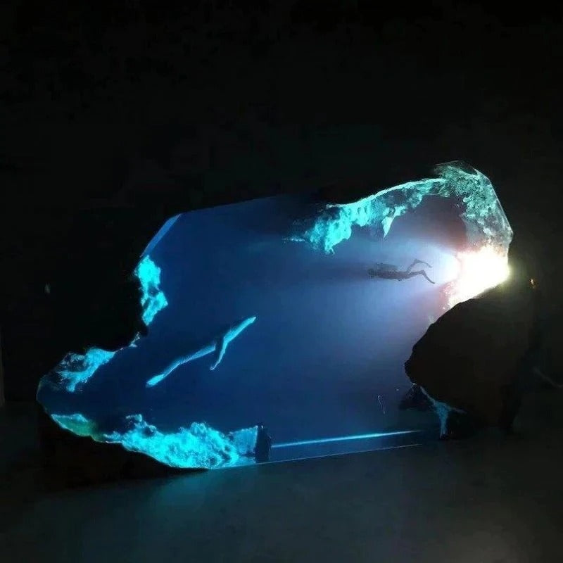 A close-up of a lamp which features a beautiful underwater scene of a diver and a humpback whale. The LED lamp is switched on and illuminates the scene in a soft blue light.