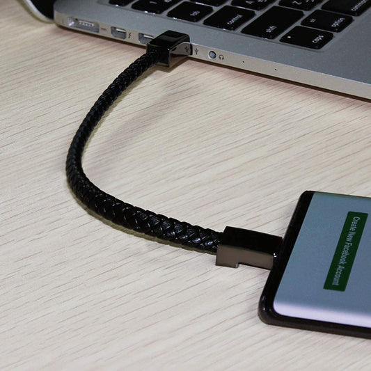 A cell phone is plugged into a laptop and is charging via a black charging wearable leather bracelet.