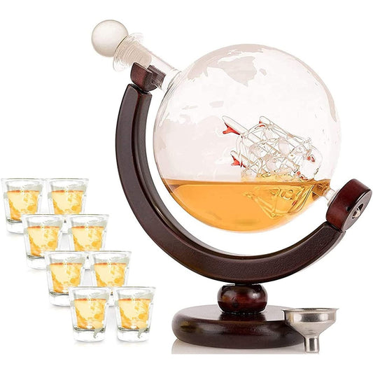 A whiskey decanter shaped like a globe with the world map etched into the glass. There is also a glass ship inside the decanter. 8 shot glasses are next to the decanter.