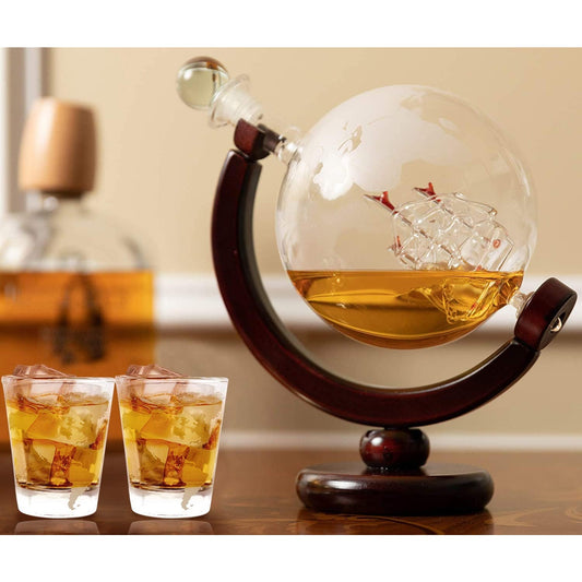 A glass whiskey decanter shaped like the world globe is filled with whiskey. There is a glass ship inside the globe and 2 shot glasses filled with whiskey next to it.