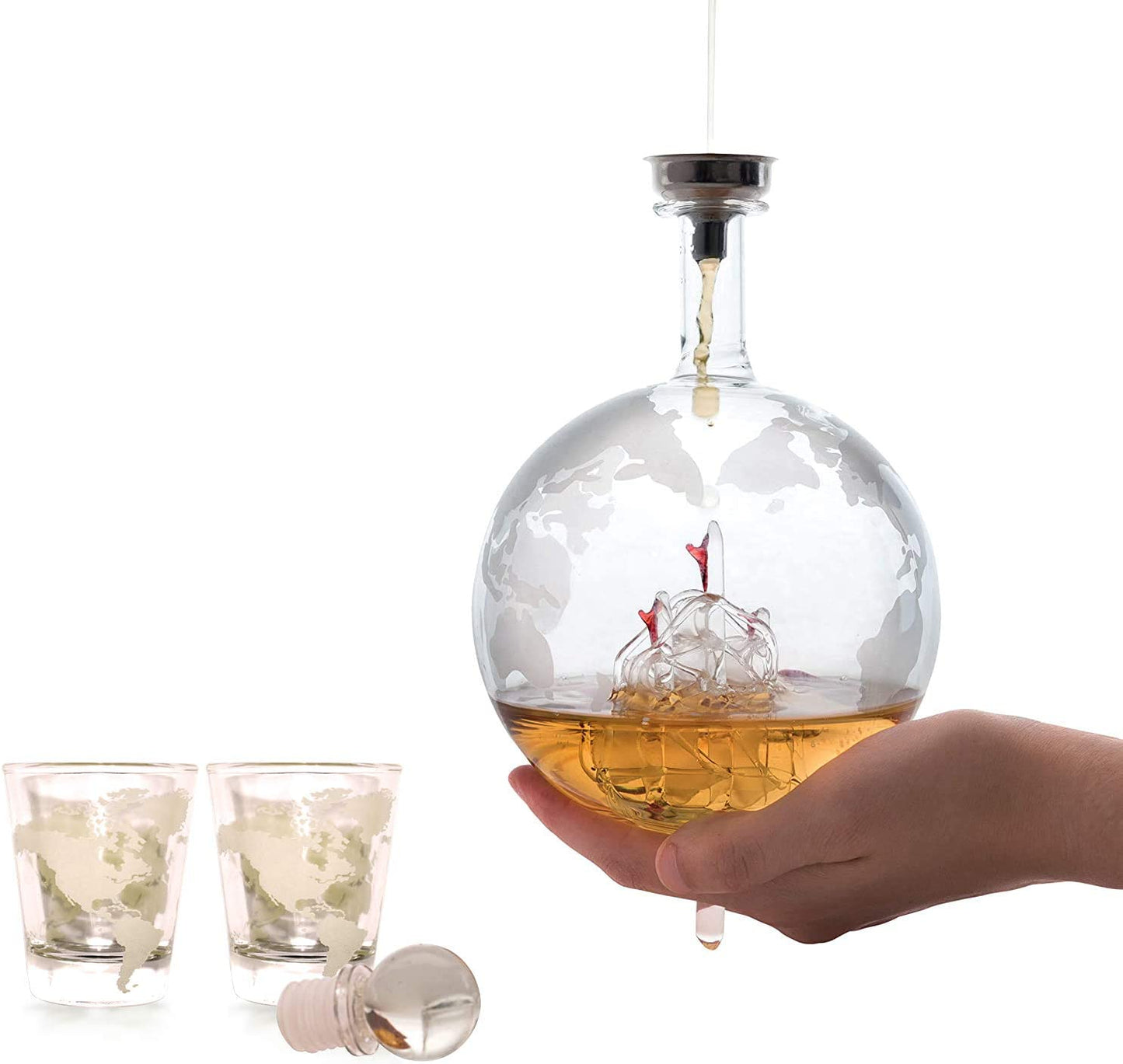 A persons hand is holding a whiskey decanter globe with a world map etched into the glass. There are 2 shot glasses nearby.