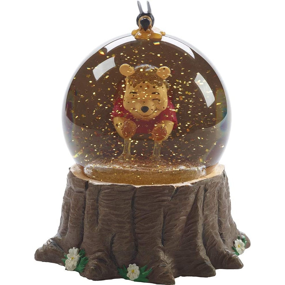 A front view of a Winnie the Pooh snow globe which shows Winnie putting his hands in a hive full of honey. The glitter swirling around looks like bees.