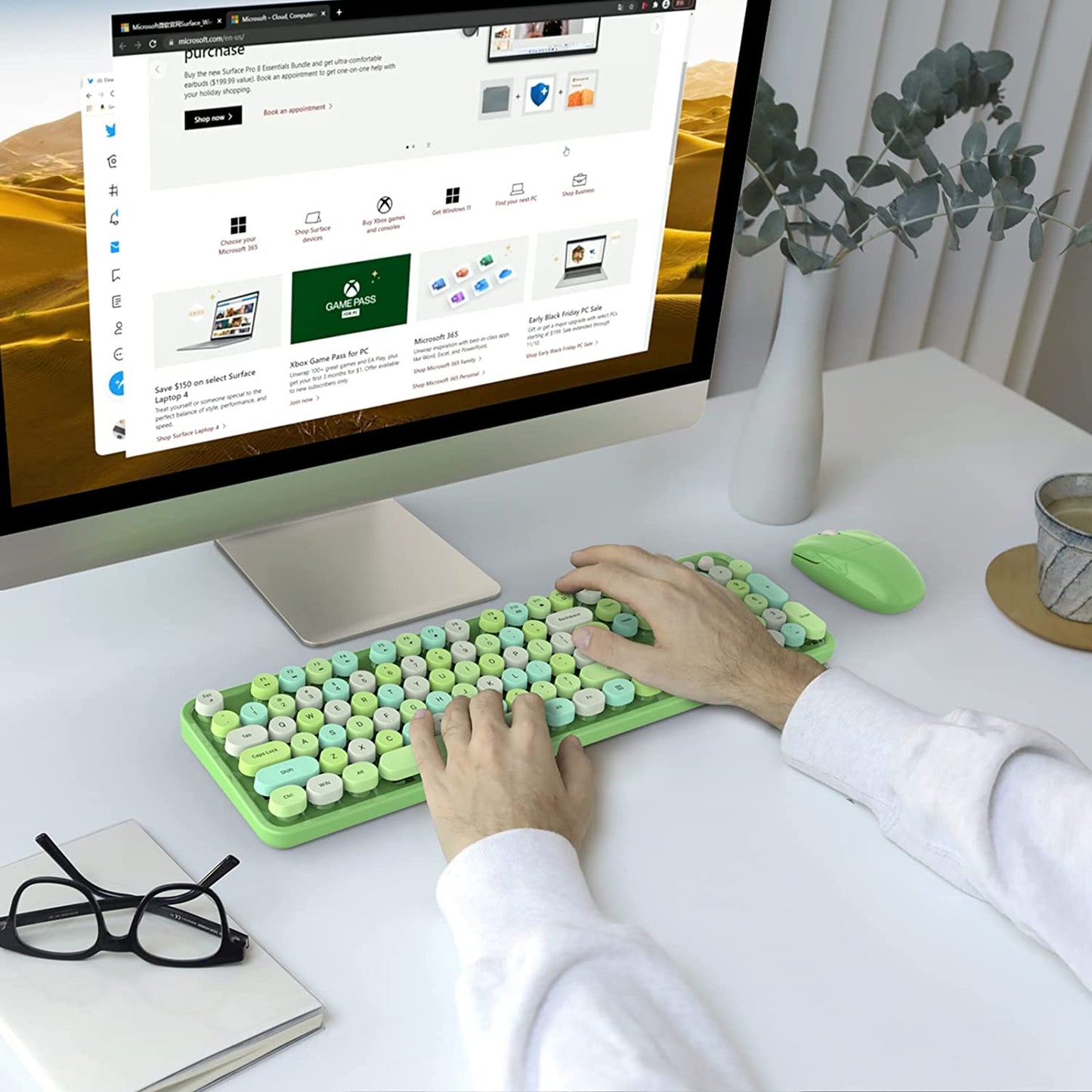 A pair of hands is typing on a green colored wireless keyboard and mouse in front of a computer screen.