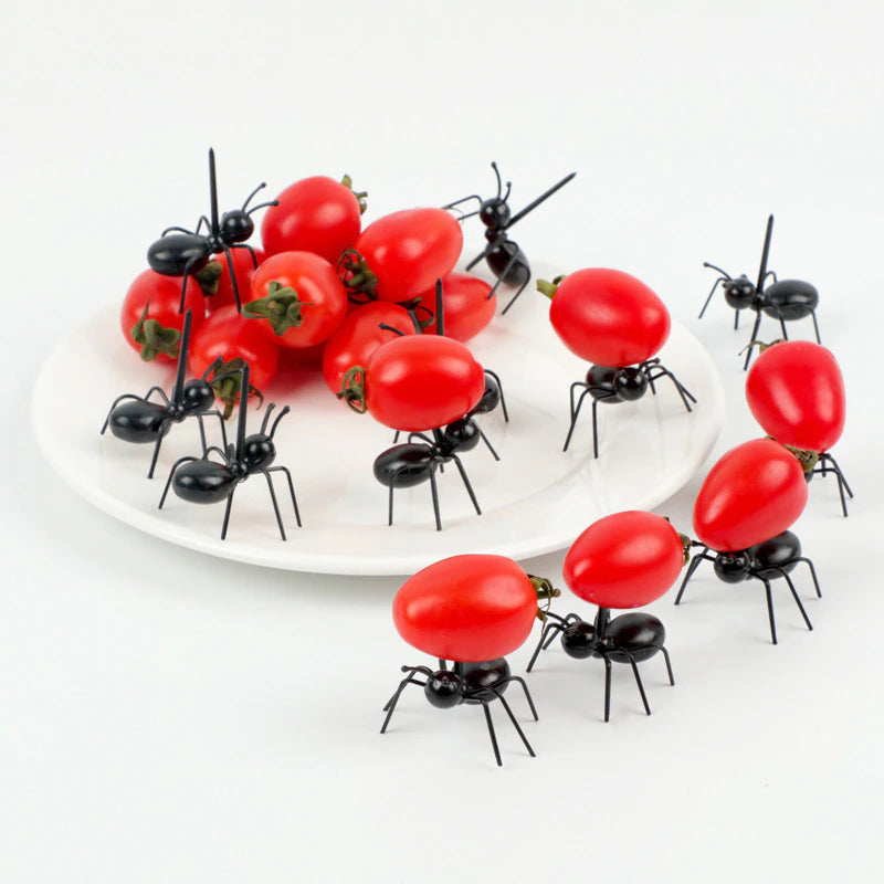 A set of 12 worker ant food picks. The plastic worker ants are decorated around and on a plate. Some are carrying cherry tomatoes while others have been set up as if they are crawling over the cherry tomatoes. 