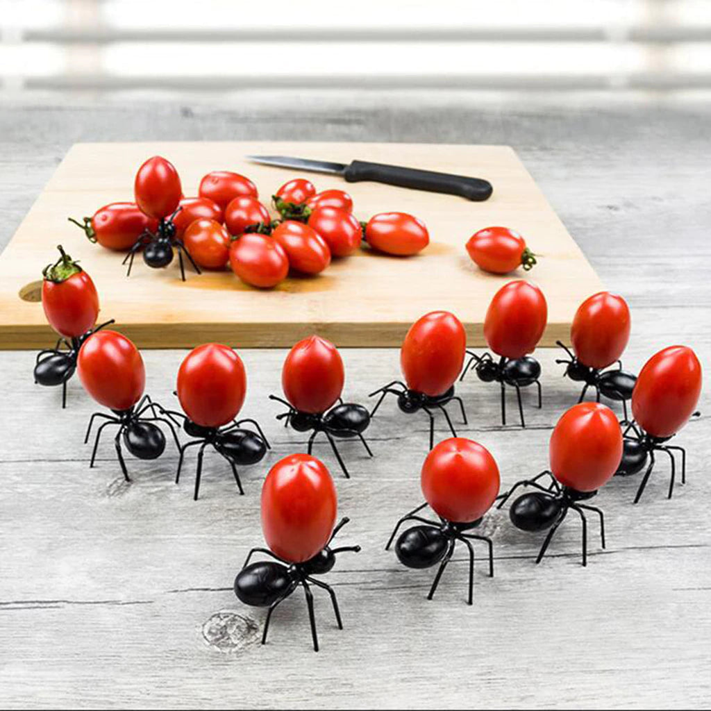 12 worker ant food picks marching one by one in an S formation. The ants are all carrying cherry tomatoes. In the background there is a chopping board with cherry tomatoes and a knife on it.