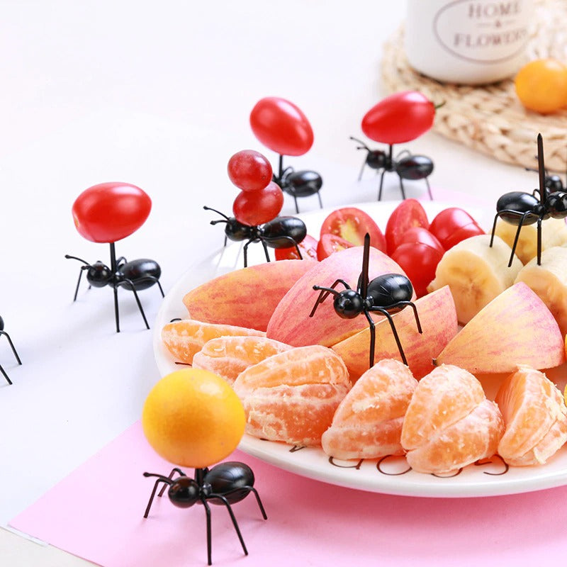 7 ant food picks set up around a plate of fruit. Some are carrying pieces of fruit and some are carrying cherry tomatoes while others are carrying nothing.
