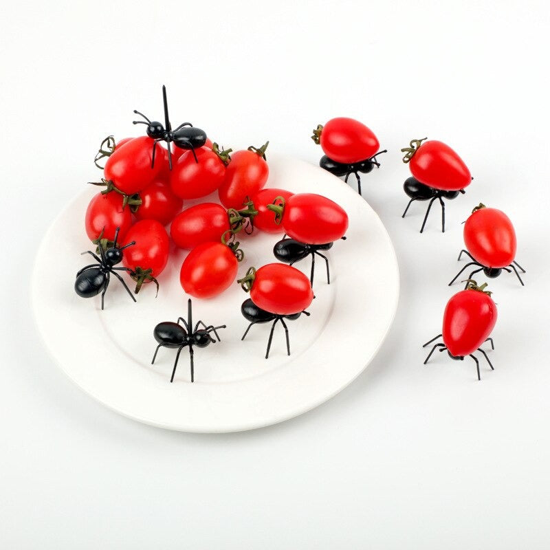 A set of 9 worker ant food picks. The plastic worker ants are decorated around and on a plate. Some are carrying cherry tomatoes while others have been set up as if they are crawling over the cherry tomatoes.